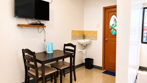 Un moderno comedor con un televisor de pantalla plana en la pared, una mesa de madera con cuatro sillas, un hervidor azul y un lavamanos blanco.
