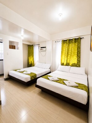 Une chambre d’hôtel avec deux lits simples, une petite fenêtre, un climatiseur fixé au mur et un sol carrelé de couleur claire.