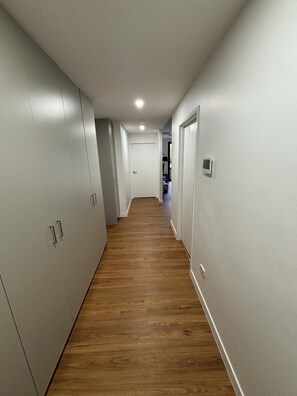 Un pasillo con piso de madera, paredes blancas y puertas a ambos lados.