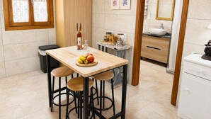 Una cocina con una mesa de madera, taburetes, una botella y un frutero.