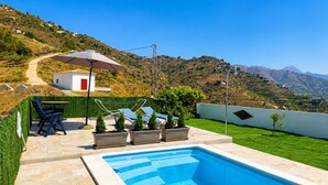 Una piscina con vistas a una colina y un edificio blanco con una puerta roja.