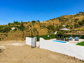 Un espace piscine avec un mur blanc, un portail et une vue sur une colline parsemée de maisons.