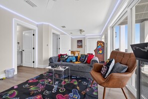 A modern living room with a sofa, gaming-themed rug, and a leather armchair. - Three-Story Home | Boat Slip | Walk Downtown (Saint Augustine)