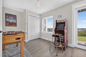 A room with a foosball table, a Pac-Man arcade machine, and a window with a view of the outdoors. - Three-Story Home | Boat Slip | Walk Downtown (Saint Augustine)
