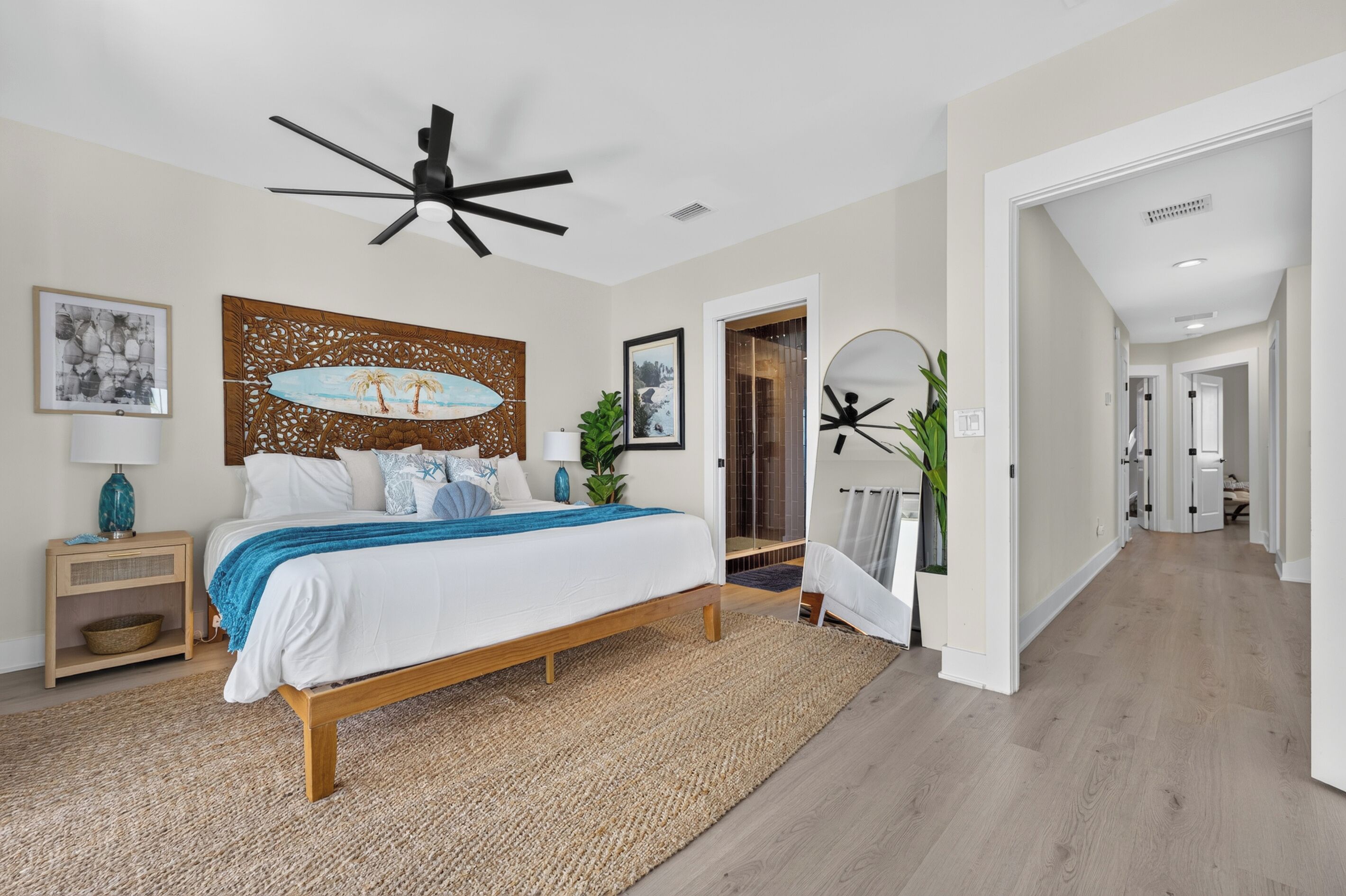 A bedroom with a bed, a ceiling fan, a wall with a decorative panel, and a hallway leading to another room.