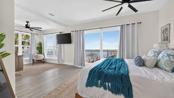 A bedroom with a bed, a ceiling fan, a TV, and a view of the outdoors.