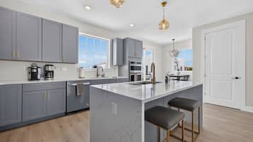 A modern kitchen with grey cabinets, a marble island, and pendant lighting.