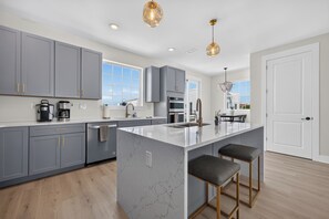 A modern kitchen with grey cabinets, a marble island, and pendant lighting.