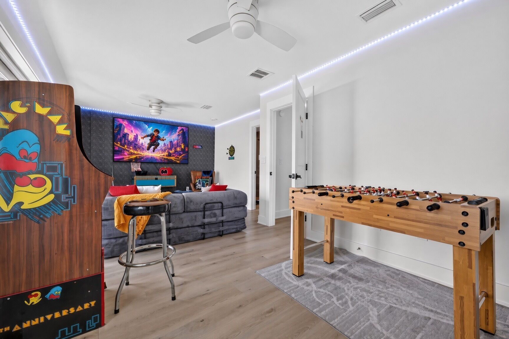 A modern living room with a foosball table, a sofa, a TV, and a decorative wall.