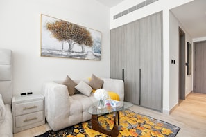 A modern living room with a sofa, a glass coffee table, and a painting of trees. - Stunning View Apartment Luxurious Living Peaceful (Dubai)