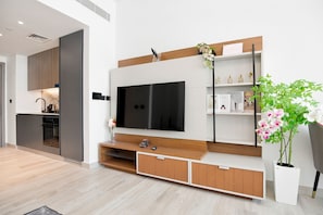 A modern living room with a large flat-screen TV, wooden accents, a kitchen in the background, and a potted orchid plant. - Stunning View Apartment Luxurious Living Peaceful (Dubai)