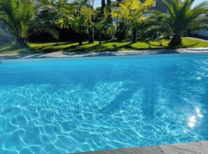 A clear swimming pool surrounded by lush greenery and palm trees. - Villa Seignosse: A Beach Vacation (Seignosse)