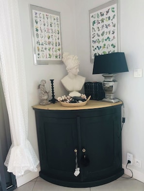 A corner room with a dark green cabinet, a bust sculpture, a framed botanical print, a lamp, and a small statue. - Villa Seignosse: A Beach Vacation (Seignosse)