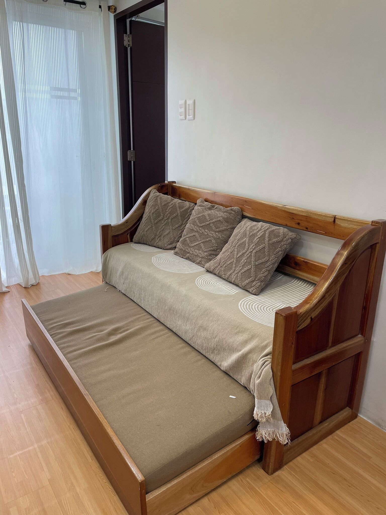 Un canapé en bois avec un matelas, deux coussins et un rideau blanc.