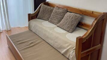 Un canapé en bois avec un matelas, deux coussins et un rideau blanc.