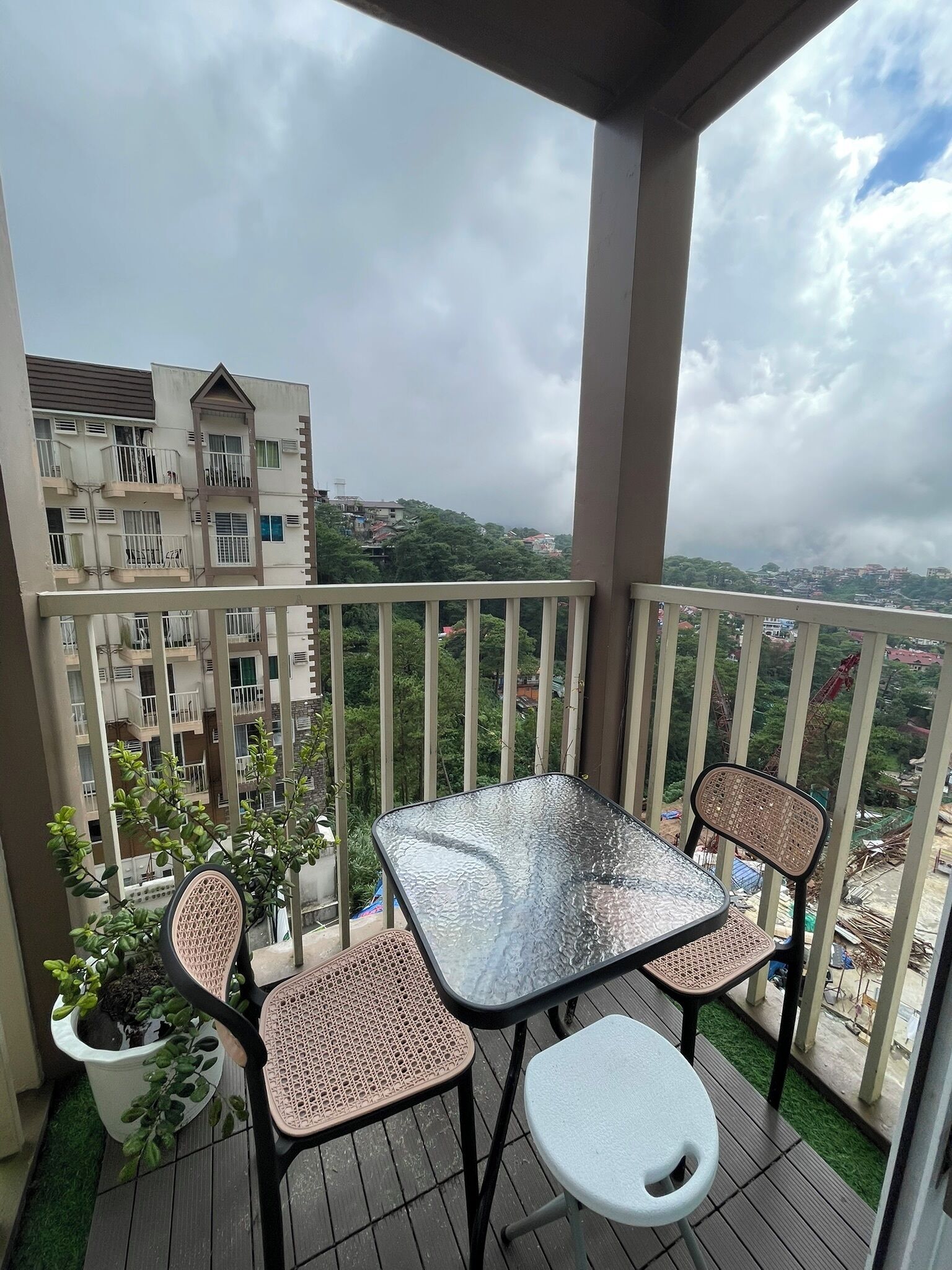 Un balcón con una mesa de vidrio y dos sillas, con vista a una zona residencial con varios edificios.