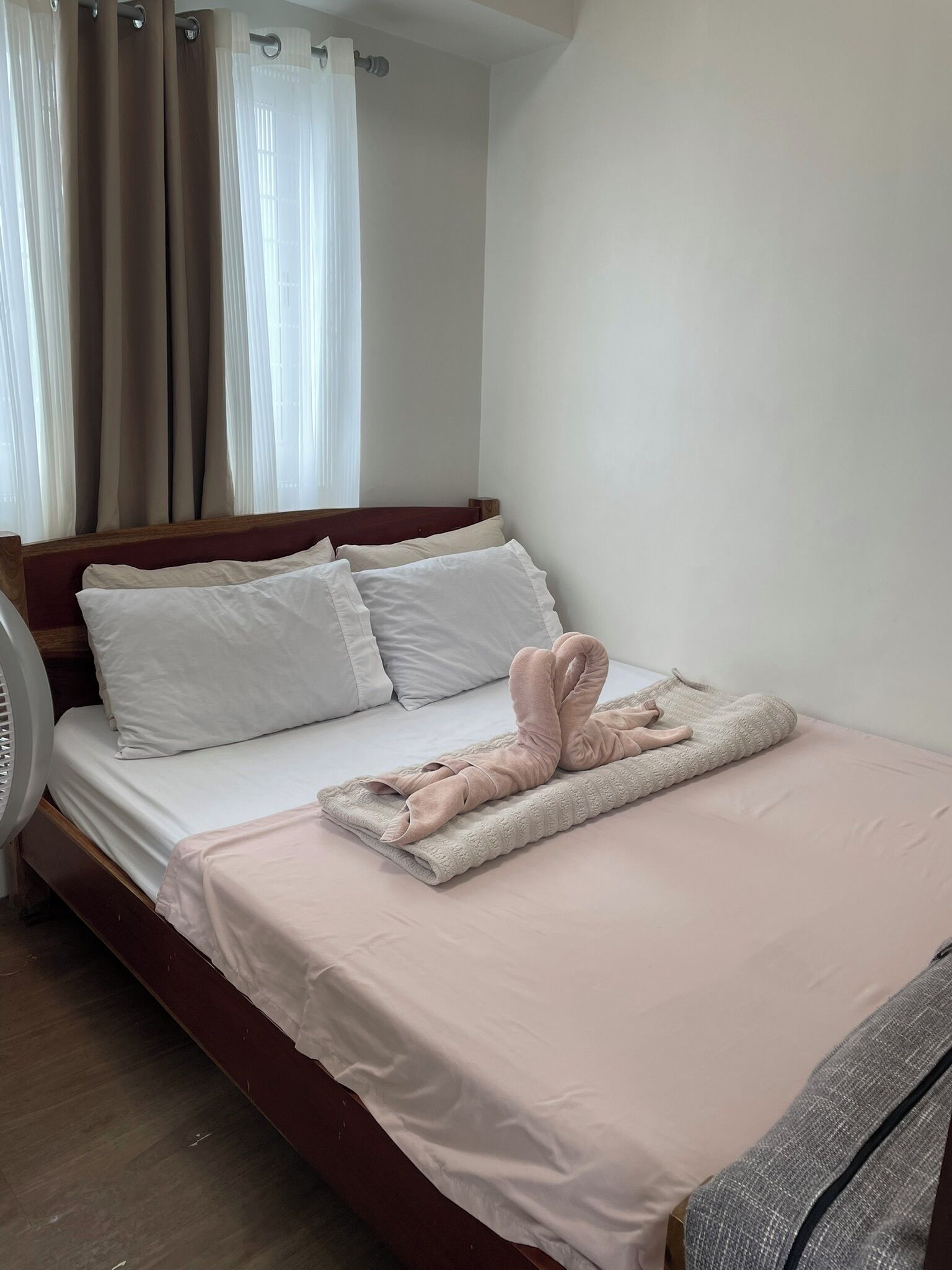 Una cama con una toalla rosa, un edredón, almohadas blancas y un ventilador junto a la cama.