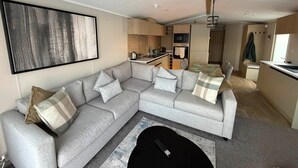 A modern living room with a grey sectional sofa, a black coffee table, and a large abstract painting on the wall. - Haggerston Castle - Lakeside Retreat (Berwick-upon-Tweed)