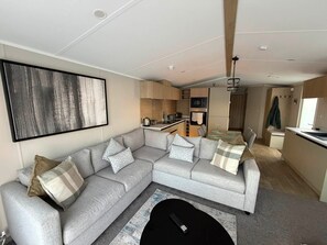 A modern living room with a grey sectional sofa, a black coffee table, and a large abstract painting on the wall. - Haggerston Castle - Lakeside Retreat (Berwick-upon-Tweed)