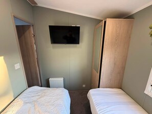 A hotel room with two beds, a television mounted on the wall, and a radiator. - Haggerston Castle - Lakeside Retreat (Berwick-upon-Tweed)