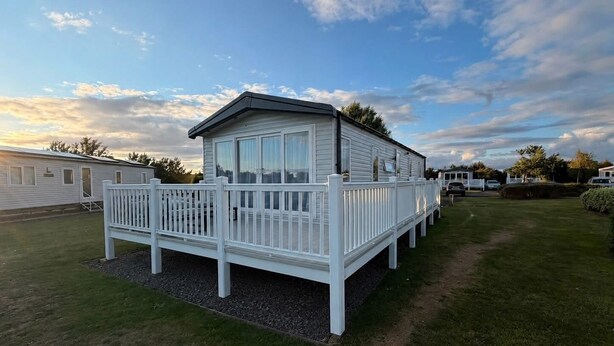 A mobile home with a fenced deck, surrounded by grass and other mobile homes. - Haggerston Castle - Lakeside Retreat (Berwick-upon-Tweed)