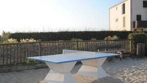 A ping pong table set up on a sandy surface with a wooden fence and a building in the background. - T2 RDC avec jardin - LACANAU OCÉAN (Lacanau)