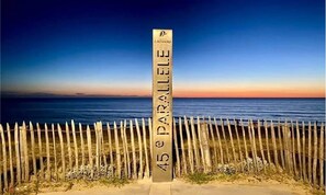 A signpost with '45 e PARALLELE' and 'LACTAMI' on it, placed in front of a wooden fence with a view of the sea and a sunset in the background. - T2 RDC avec jardin - LACANAU OCÉAN (Lacanau)