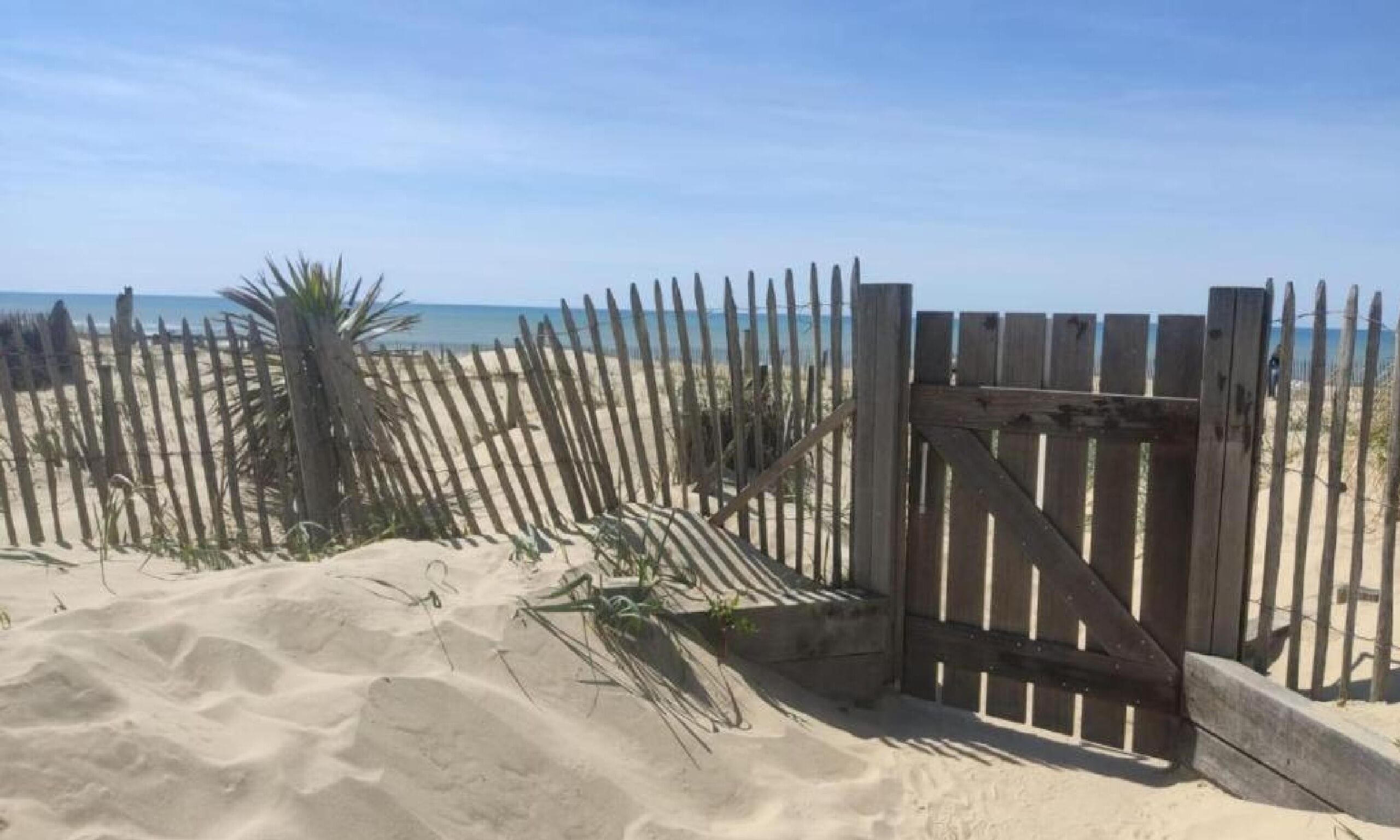 Une plage de sable avec une clôture et une porte en bois.