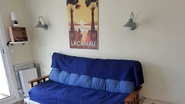 A living room with a blue sofa, a wooden dining table, and a chair. - T2 RDC avec jardin - LACANAU OCÉAN (Lacanau)