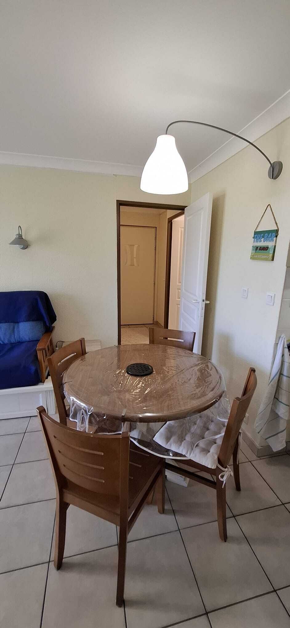 A dining area with a round table, six chairs, a hanging light fixture, and a door in the background.