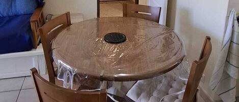 A dining area with a round table, six chairs, a hanging light fixture, and a door in the background.
