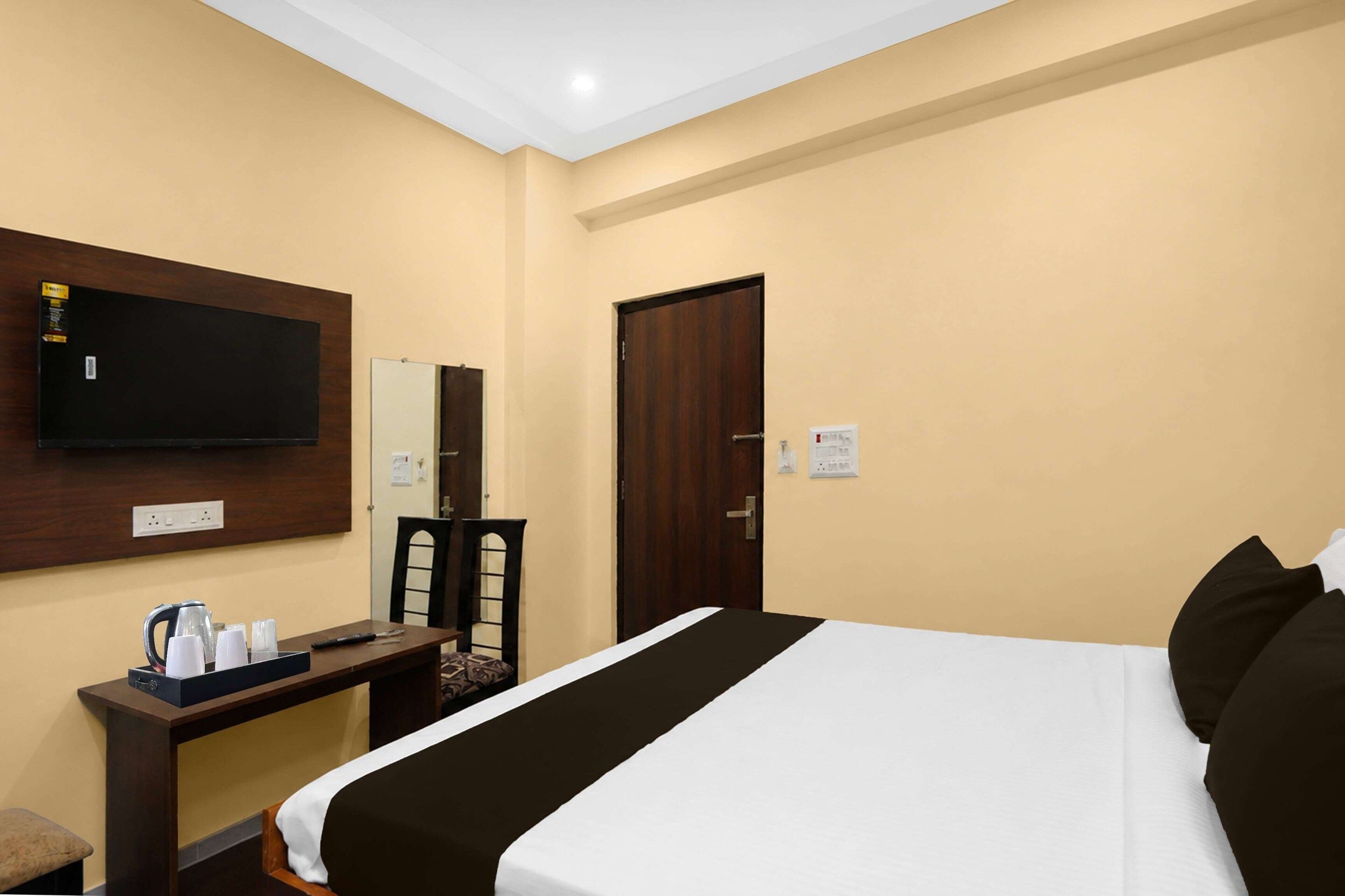 Una habitación de hotel con una cama, un escritorio con televisor de pantalla plana, una silla y una puerta.
