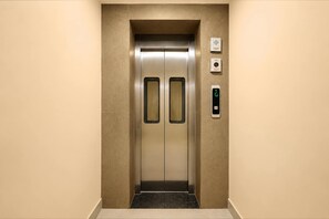 Ein Aufzug mit metallischer Oberfläche, Bedienfeld mit digitaler Anzeige und einem wandmontierten Gegensprechanlage.