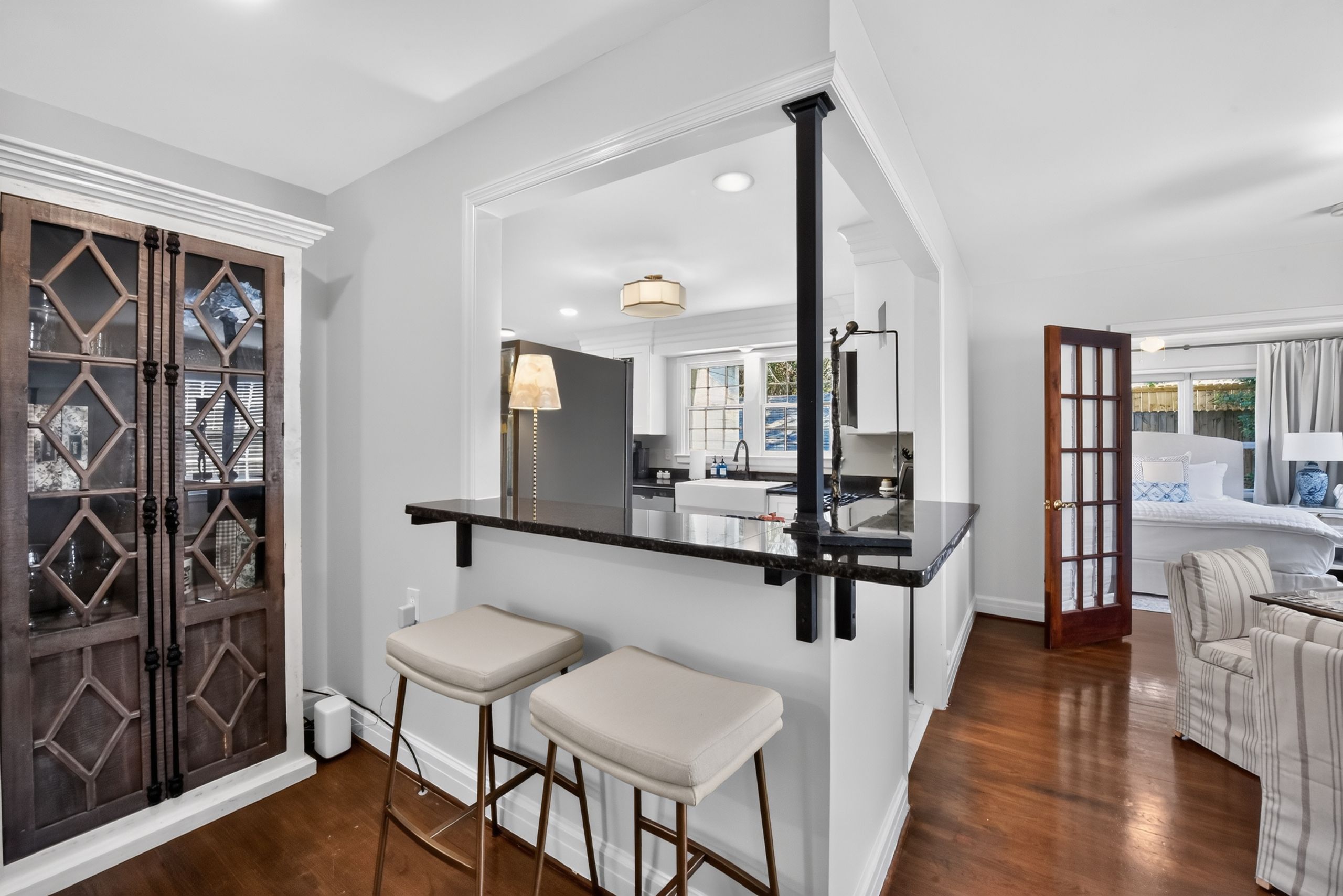 A modern kitchen with a bar area, two bar stools, and a view into the adjacent living room.