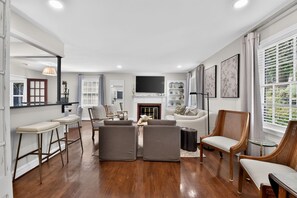 A modern living room with a fireplace, seating area, and a television. - Capstone Cottage | Walk to Bryant-Denny Stadium | 3 King Beds (Tuscaloosa)