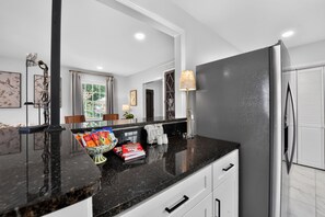 Una cocina moderna con encimera de granito negro, armarios blancos y un refrigerador de acero inoxidable.