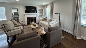 A modern living room with a fireplace, a sofa, a coffee table, and a television. - Capstone Cottage | Walk to Bryant-Denny Stadium | 3 King Beds (Tuscaloosa)