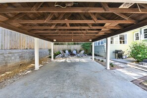 Un espacio de patio cubierto al aire libre con piso de concreto, vigas de madera y sillas tipo Adirondack.