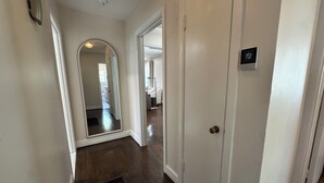 A hallway with a white door, a mirror, and a thermostat. - Capstone Cottage | Walk to Bryant-Denny Stadium | 3 King Beds (Tuscaloosa)