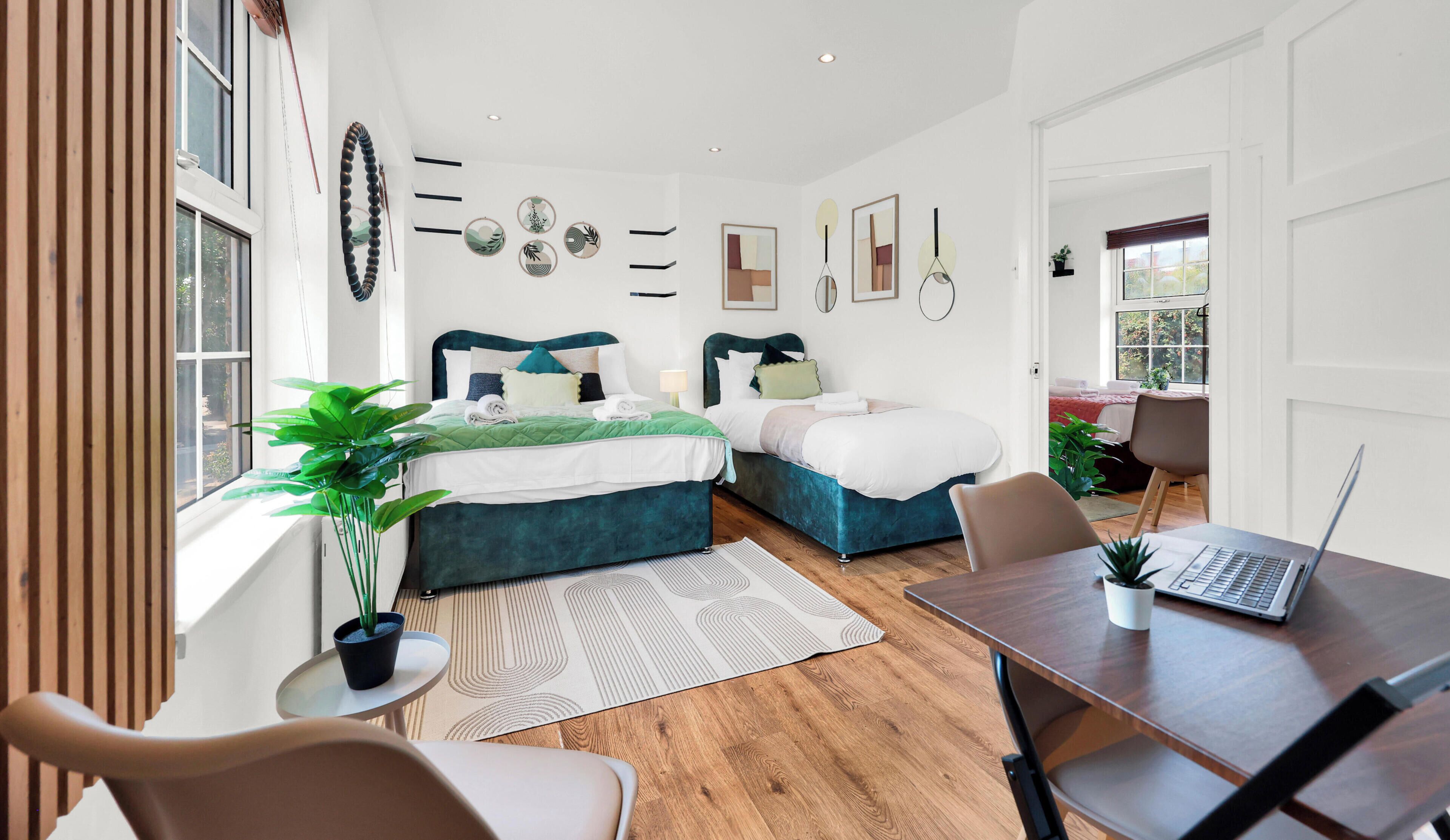 A modern bedroom with two beds, a desk, and a laptop.