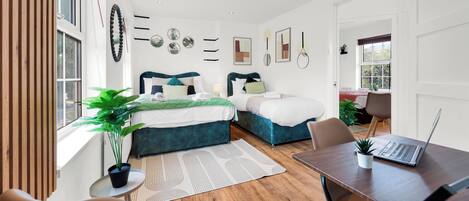 A modern bedroom with two beds, a desk, and a laptop.