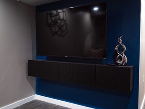 A modern entertainment unit with a flat-screen TV mounted on a wall, a dark wood cabinet below, and a decorative metal sculpture to the right. - Private Basement Retreat in South Bend 10 min from Notre Dame (South Bend)