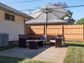 Une terrasse à l’arrière de la maison, avec des meubles d’extérieur, un grand parasol et une clôture en bois.