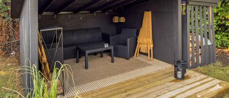 Een terras met een houten dek, een bank, een tafel en een stoel.