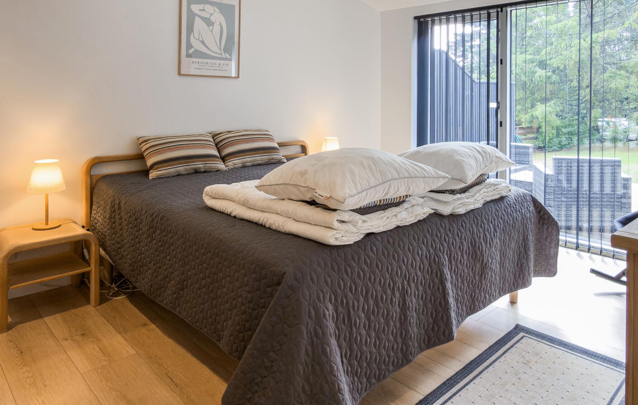 Een net opgemaakt bed met een gewatteerde deken, twee bedlampen en een lijst met kunstwerk aan de muur.