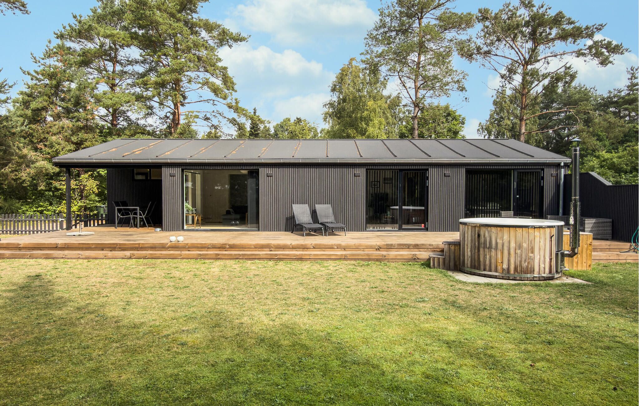 En moderne bygning med fladt tag, store vinduer og en overdækket patio med udendørs siddepladser.