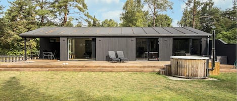 En moderne bygning med fladt tag, store vinduer og en overdækket patio med udendørs siddepladser.