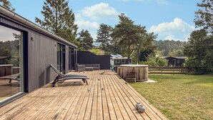 A wooden deck with a glass door leading to a modern building, a hot tub, and a grassy area with trees. - 3 bedroom amazing home in Ebeltoft (Ebeltoft)