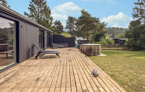 A wooden deck with a glass door leading to a modern building, a hot tub, and a grassy area with trees. - 3 bedroom amazing home in Ebeltoft (Ebeltoft)