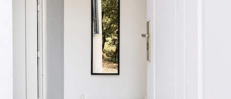 A narrow hallway with a bench, a door, and a mirror reflecting a tree outside.